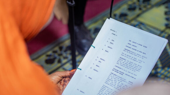 A view over a woman's shoulder as she holds sheets of paper printed with a radio script.